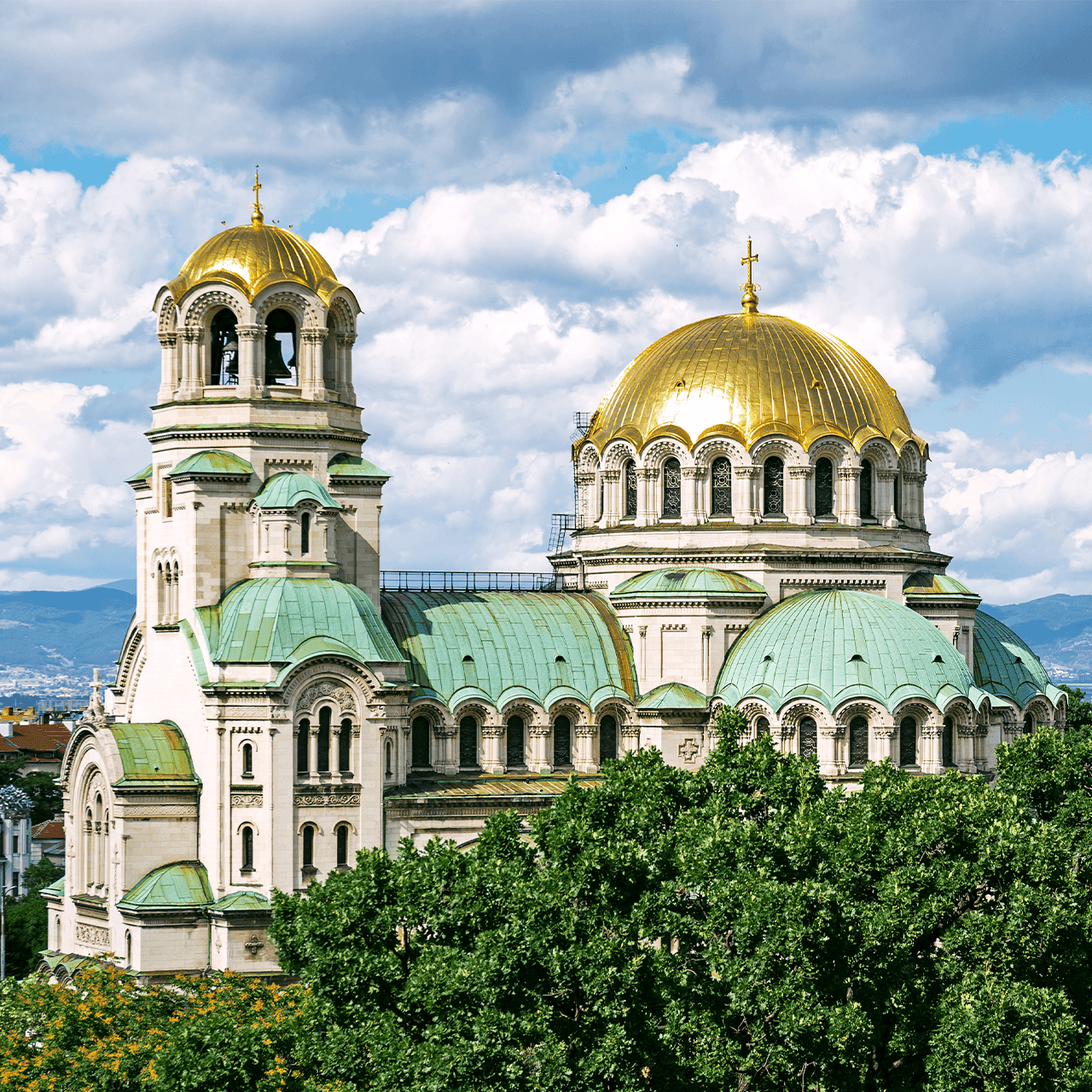 Ornate cathedral with golden domes and green roofs under a partly cloudy sky.