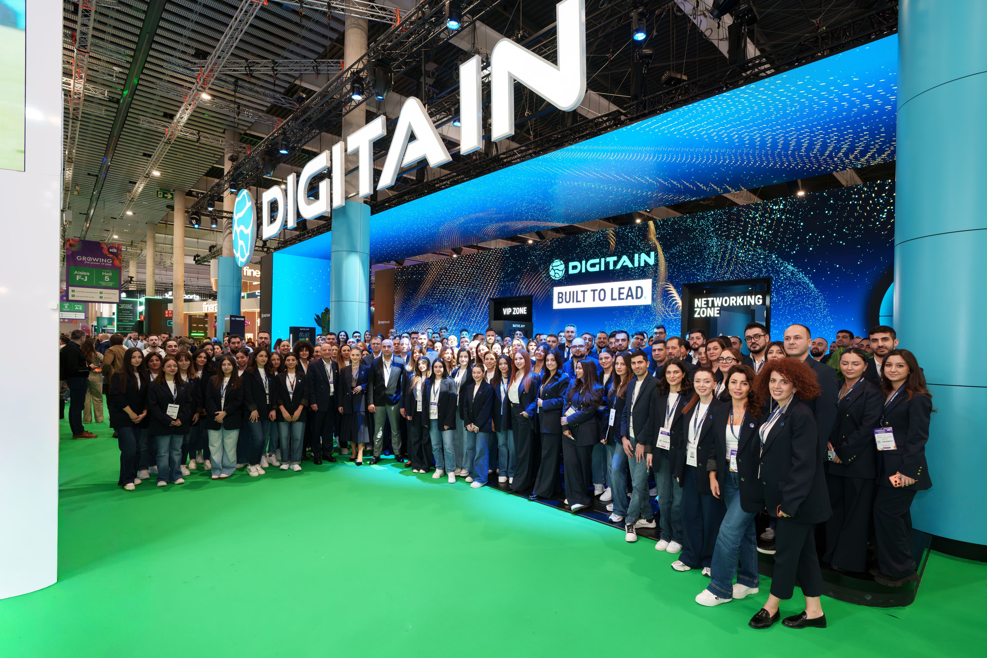Large group of Digitain employees posing at their modern, branded trade show booth.