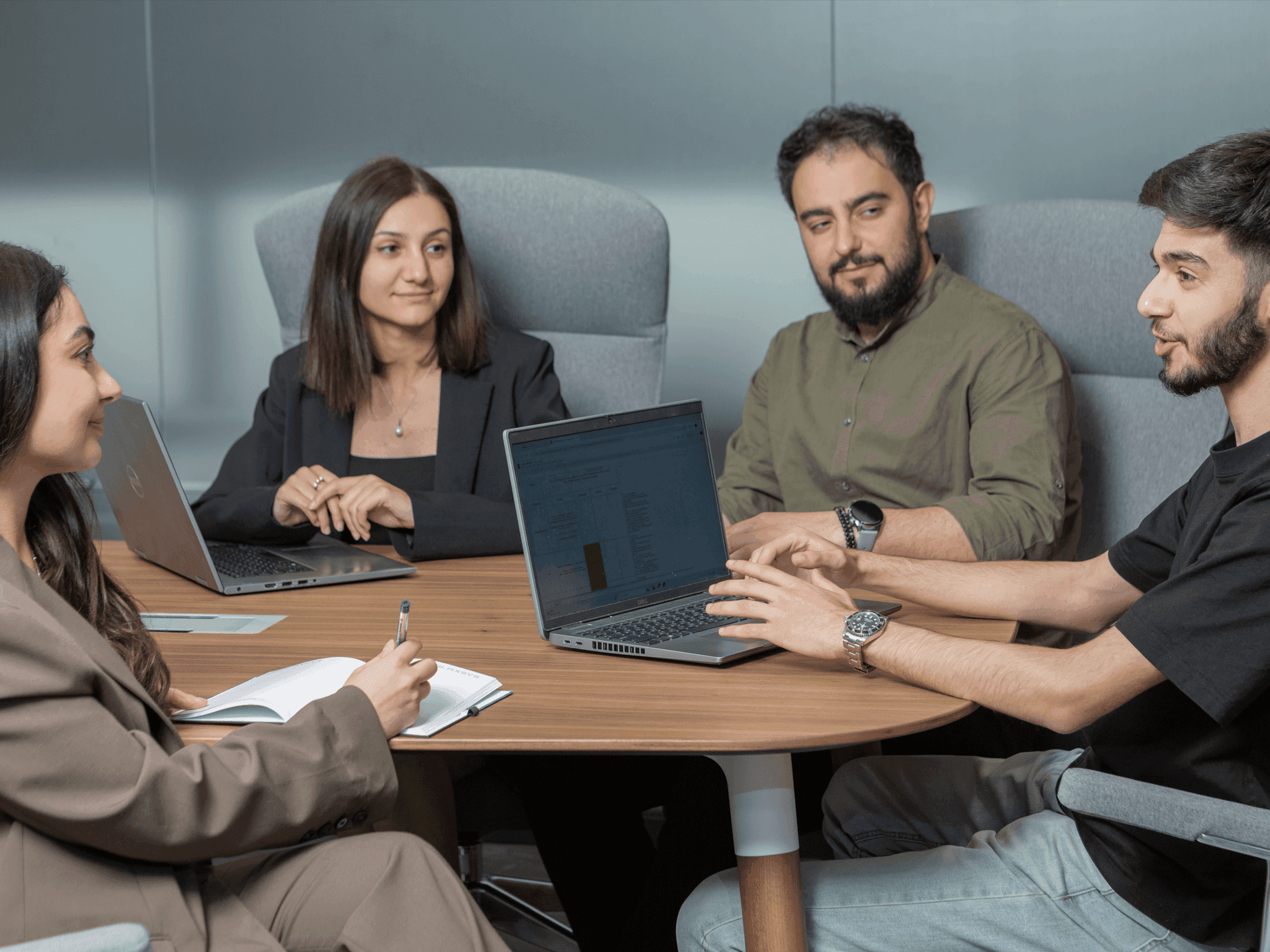 Four diverse professionals collaborate around a table with laptops in a modern office.