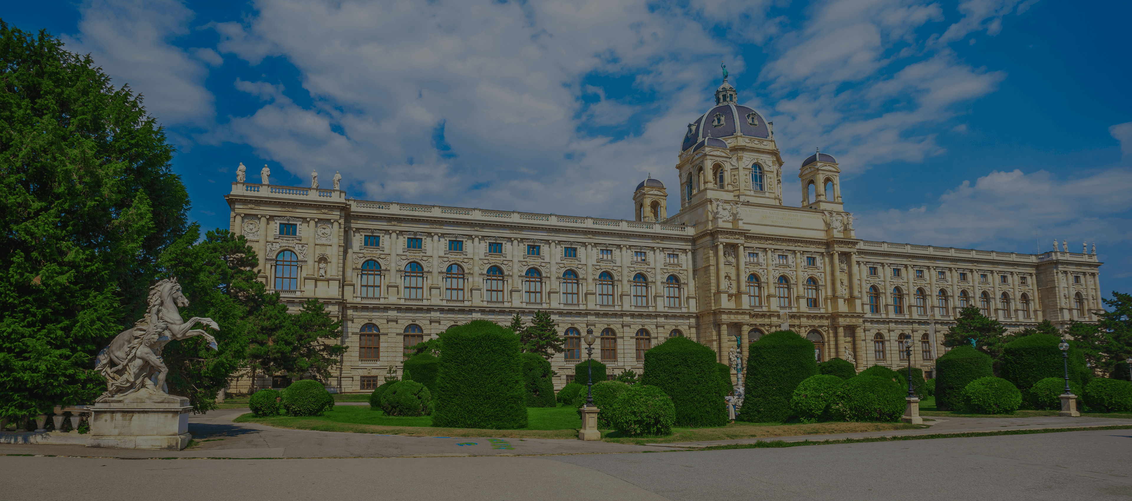 Large ornate museum building with a dome, formal gardens, and a rearing horse statue.