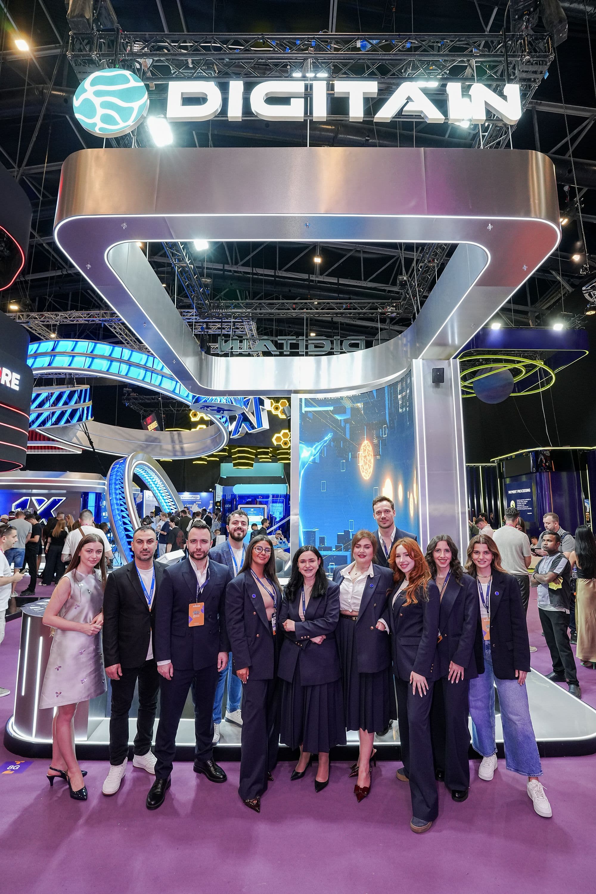 A group of professionals stands smiling in front of a modern Digitain exhibition booth.