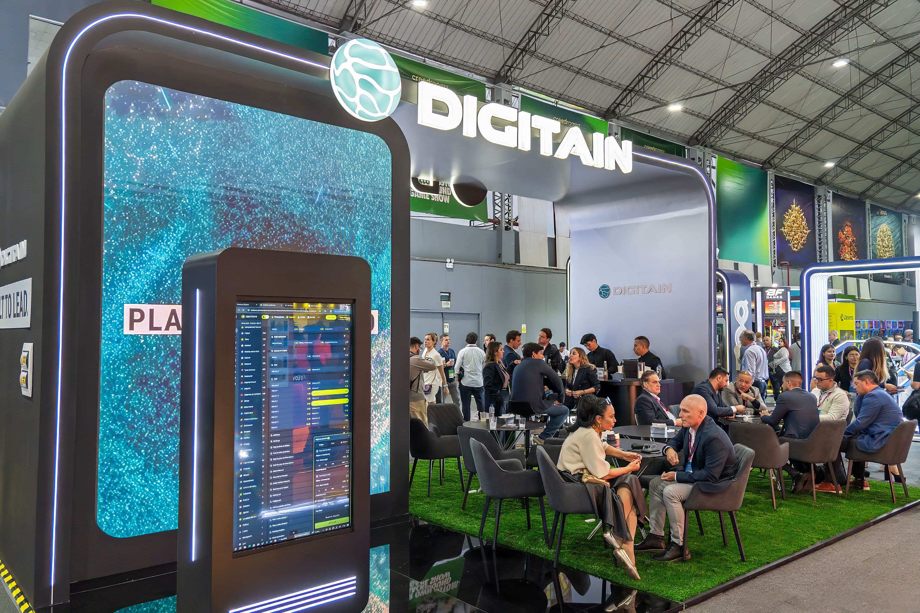 Modern Digitain exhibition booth featuring large digital screens and people networking in a lounge area.