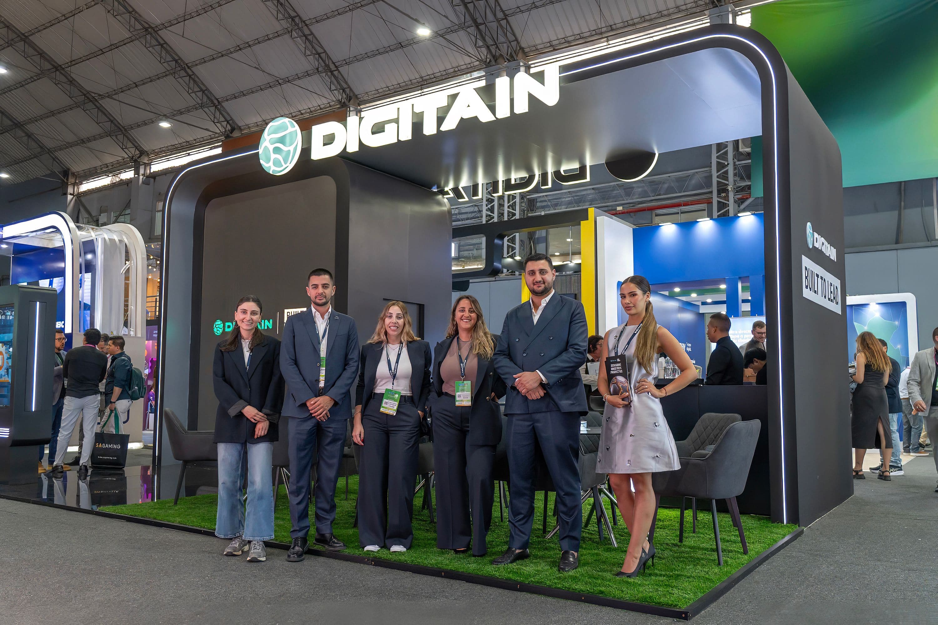 Six professionals pose in front of a modern DIGITAIN exhibition booth at a trade show.